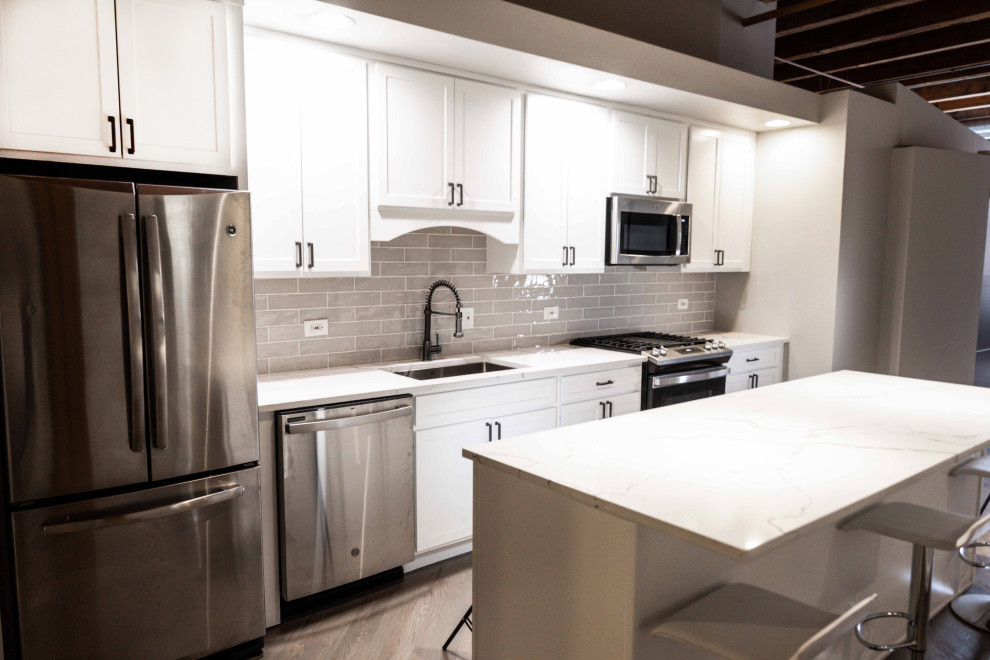 Contemporary single-wall kitchen in Chicago with an undermount sink, recessed-panel cabinets, white cabinets, quartzite benchtops, grey splashback, with island and white benchtop.