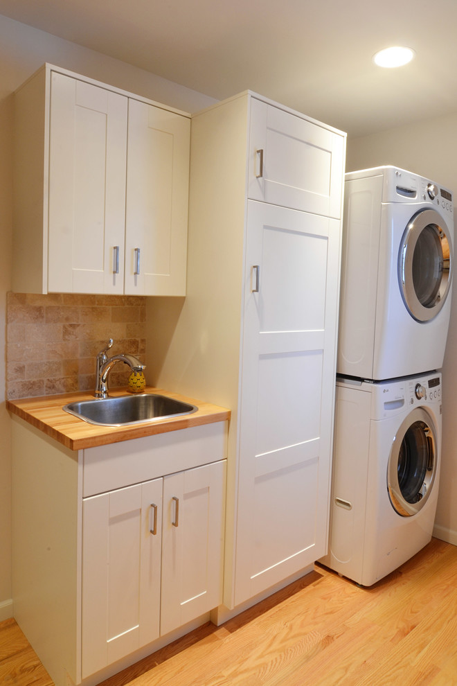 Inspiration for a small transitional galley utility room in Other with a drop-in sink, shaker cabinets, white cabinets, wood benchtops, grey walls, light hardwood floors and a stacked washer and dryer.