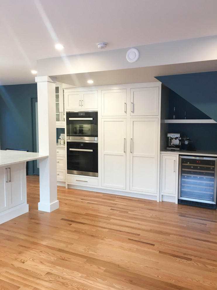 Example of a large transitional u-shaped light wood floor and beige floor eat-in kitchen design with a double-bowl sink, shaker cabinets, white cabinets, quartzite countertops, white backsplash, subway tile backsplash, stainless steel appliances, an island and white countertops