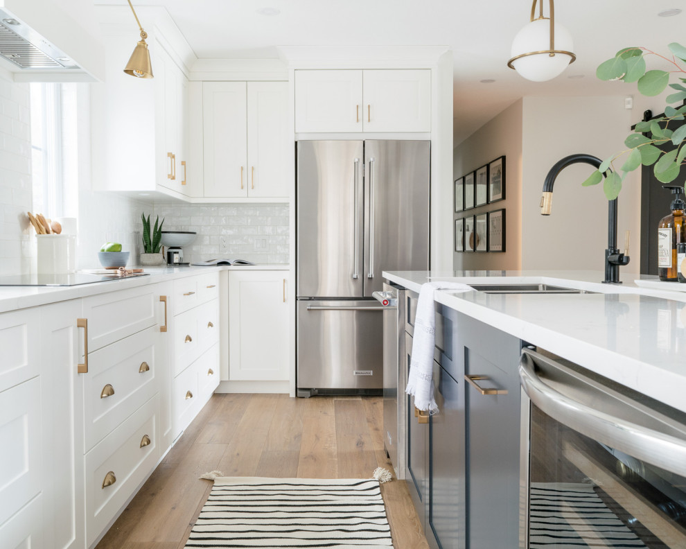 Large transitional l-shaped medium tone wood floor and brown floor eat-in kitchen photo with a triple-bowl sink, shaker cabinets, white cabinets, quartz countertops, white backsplash, subway tile backsplash, stainless steel appliances, an island and white countertops