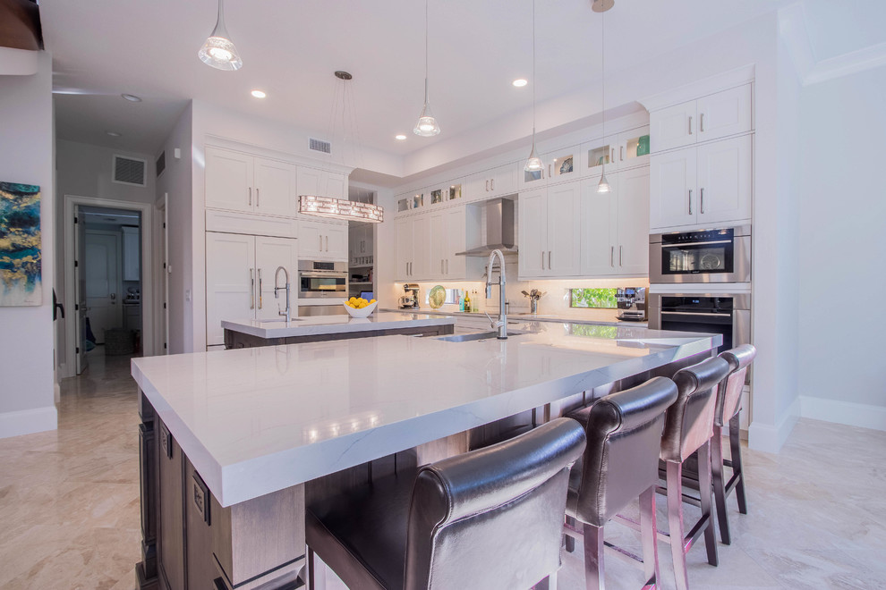 Open concept kitchen - huge transitional l-shaped porcelain tile and beige floor open concept kitchen idea with a farmhouse sink, shaker cabinets, white cabinets, quartz countertops, white backsplash, porcelain backsplash, stainless steel appliances and two islands