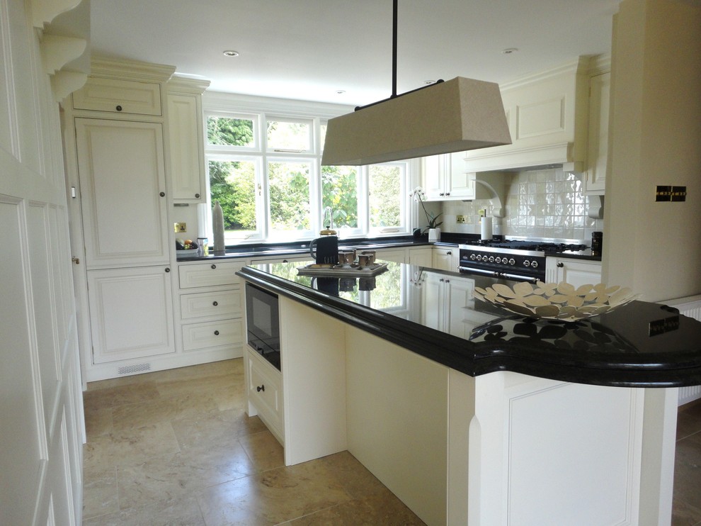 Photo of a traditional eat-in kitchen in West Midlands with a double-bowl sink, raised-panel cabinets, white cabinets, granite benchtops, white splashback, ceramic splashback, black appliances, limestone floors and with island.