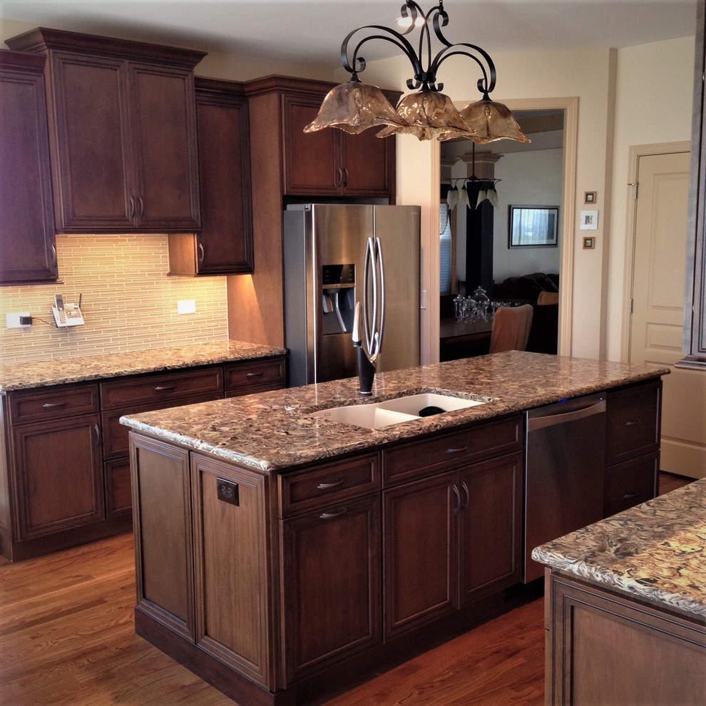 Example of a mid-sized transitional medium tone wood floor and brown floor eat-in kitchen design in Chicago with a double-bowl sink, recessed-panel cabinets, brown cabinets, quartz countertops, beige backsplash, glass sheet backsplash, stainless steel appliances and an island