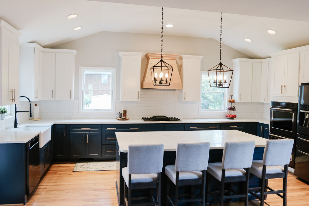 Inspiration for a large modern u-shaped eat-in kitchen in Baltimore with a farmhouse sink, shaker cabinets, blue cabinets, quartz benchtops, white splashback, subway tile splashback, stainless steel appliances, medium hardwood floors, with island, brown floor, white benchtop and vaulted.
