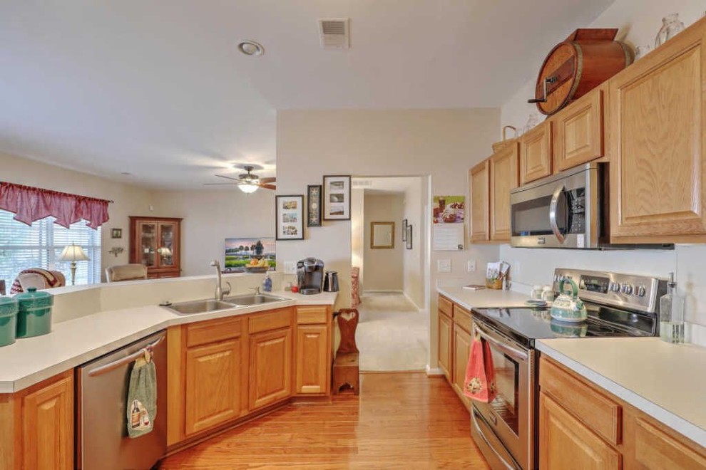 Example of a mid-sized u-shaped medium tone wood floor and brown floor kitchen design in Charleston with an undermount sink, raised-panel cabinets, beige cabinets, granite countertops, brown backsplash, ceramic backsplash, stainless steel appliances and beige countertops