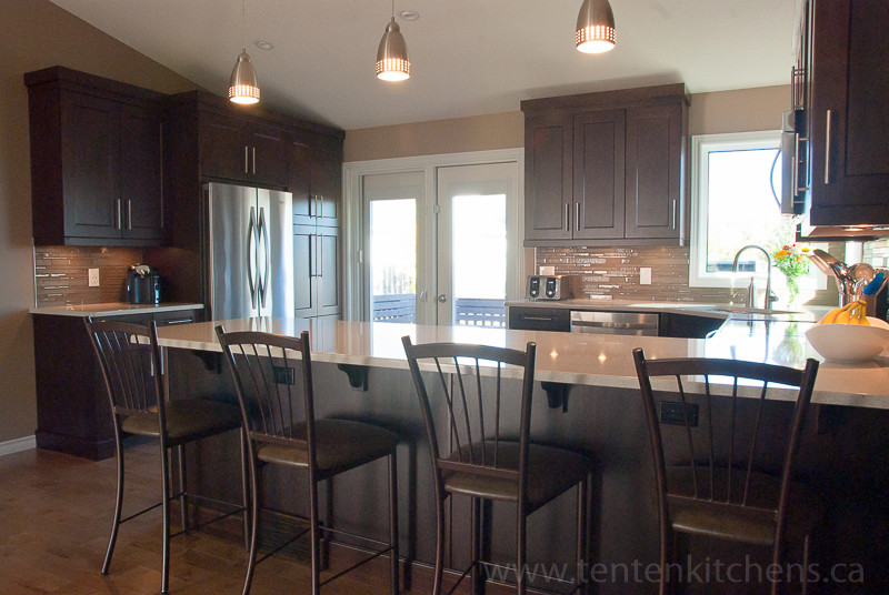 Mid-sized transitional u-shaped light wood floor open concept kitchen photo with an undermount sink, shaker cabinets, dark wood cabinets, quartz countertops, brown backsplash, glass tile backsplash, stainless steel appliances and a peninsula