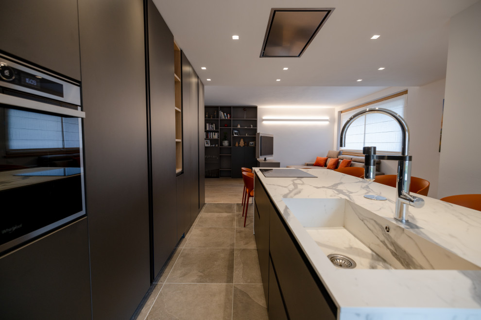 Large modern galley open plan kitchen in Milan with an integrated sink, flat-panel cabinets, black cabinets, laminate benchtops, stainless steel appliances, porcelain floors, multiple islands, multi-coloured floor, white benchtop and recessed.