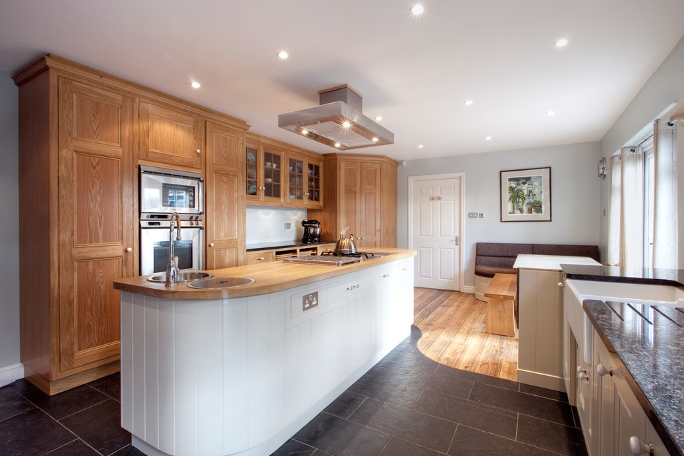 This is an example of a mid-sized country single-wall open plan kitchen in London with a double-bowl sink, recessed-panel cabinets, medium wood cabinets, wood benchtops, white splashback, glass sheet splashback, stainless steel appliances, ceramic floors and with island.