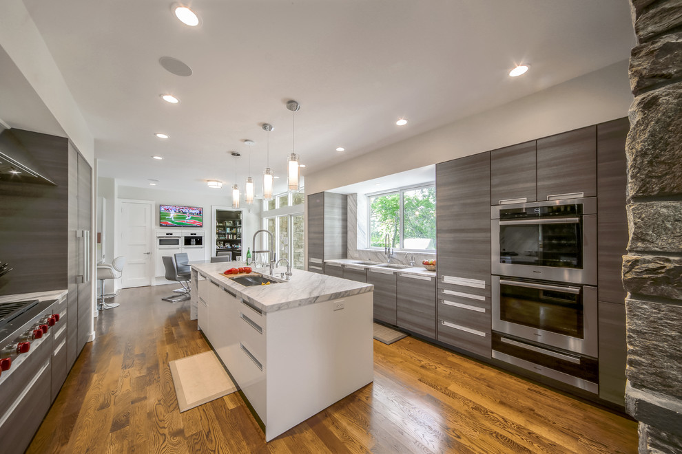 Large modern kitchen in New York with an undermount sink, flat-panel cabinets, medium wood cabinets, marble benchtops, grey splashback, marble splashback, stainless steel appliances, light hardwood floors, with island and brown floor.
