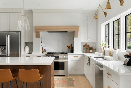 Bright white Shaker kitchen with long brushed brass bar pulls on drawers, matching knobs on doors, quartz counters, stainless appliances, and black-framed windows
