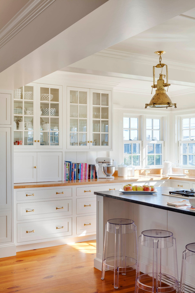 Design ideas for a large beach style u-shaped open plan kitchen in Providence with beaded inset cabinets, white cabinets, white splashback, light hardwood floors, a farmhouse sink, wood benchtops, stainless steel appliances and with island.