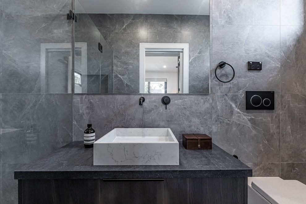 This is an example of a large modern master bathroom in Sydney with dark wood cabinets, a freestanding tub, beige tile, ceramic tile, white walls, cement tiles, marble benchtops, grey floor, an open shower, black benchtops, a single vanity and a floating vanity.