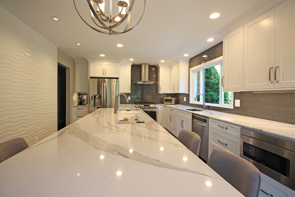 Inspiration for a mid-sized transitional l-shaped eat-in kitchen in Detroit with an undermount sink, shaker cabinets, white cabinets, quartz benchtops, grey splashback, glass tile splashback, stainless steel appliances, dark hardwood floors, with island, brown floor and white benchtop.