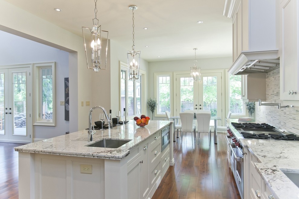 Eat-in kitchen - large transitional galley medium tone wood floor and brown floor eat-in kitchen idea in Toronto with an undermount sink, shaker cabinets, white cabinets, granite countertops, white backsplash, glass tile backsplash, stainless steel appliances and an island