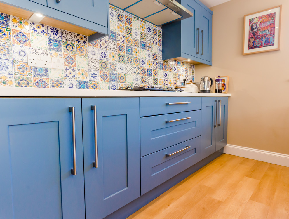 This is an example of a mid-sized contemporary u-shaped eat-in kitchen in London with an undermount sink, shaker cabinets, blue cabinets, quartz benchtops, blue splashback, mosaic tile splashback, stainless steel appliances, laminate floors, a peninsula and beige floor.