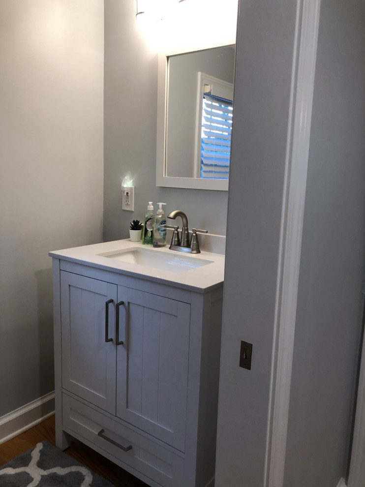 Inspiration for a small classic bathroom in Bridgeport with recessed-panel cabinets, grey cabinets, a one-piece toilet, grey walls, light hardwood flooring, a submerged sink, engineered stone worktops, brown floors, white worktops, a laundry area, a single sink and a freestanding vanity unit.