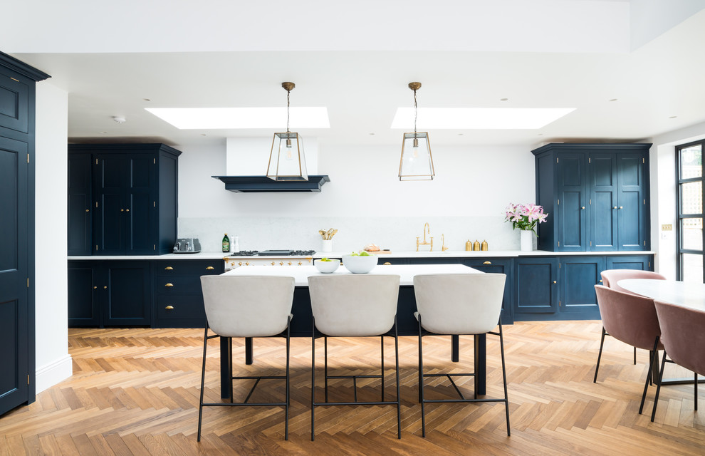 Photo of an expansive transitional galley eat-in kitchen in London with a drop-in sink, blue cabinets, marble benchtops, white splashback, marble splashback, white appliances, white benchtop, shaker cabinets, medium hardwood floors, with island and beige floor.