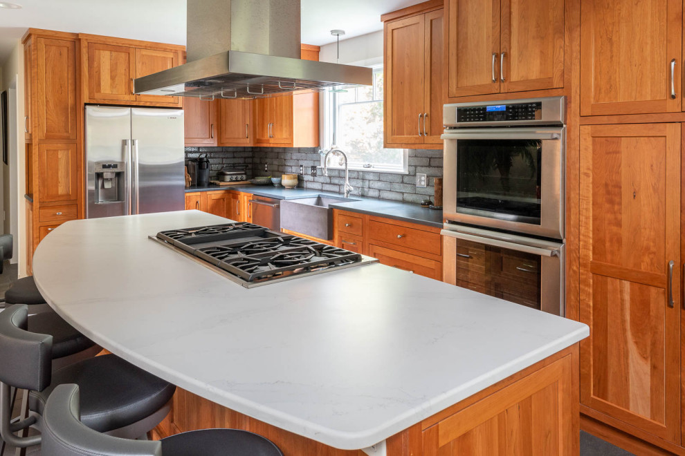 Inspiration for a large transitional l-shaped porcelain tile and gray floor eat-in kitchen remodel in Boston with a farmhouse sink, shaker cabinets, medium tone wood cabinets, quartz countertops, gray backsplash, porcelain backsplash, stainless steel appliances, an island and white countertops