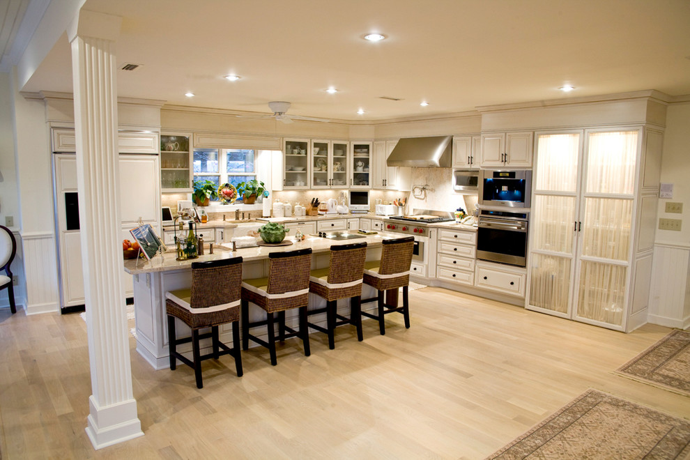 Example of a large transitional l-shaped light wood floor kitchen design with a farmhouse sink, raised-panel cabinets, beige cabinets, granite countertops, beige backsplash, paneled appliances, an island and stone slab backsplash