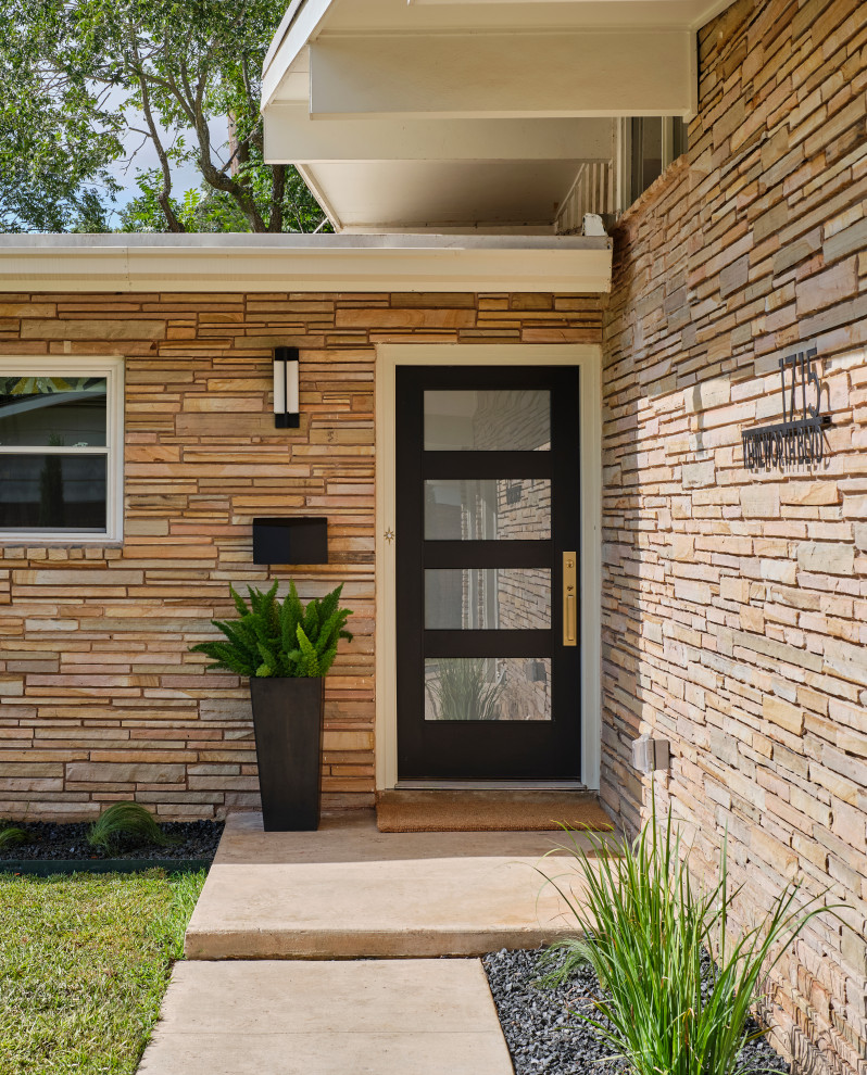 Design ideas for a mid-sized midcentury one-storey beige house exterior in Austin with stone veneer, a flat roof, a mixed roof and a black roof.