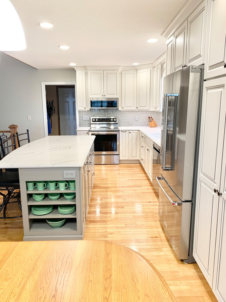 Inspiration for a transitional l-shaped open plan kitchen in Other with an undermount sink, raised-panel cabinets, white cabinets, quartz benchtops, blue splashback, subway tile splashback, stainless steel appliances, light hardwood floors, with island, brown floor and white benchtop.