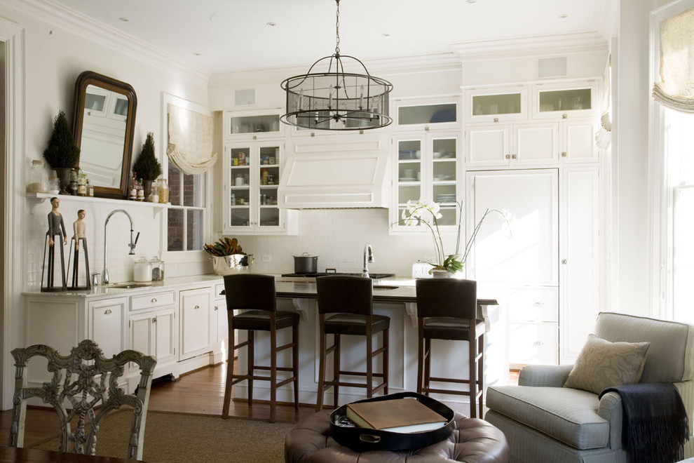 This is an example of a traditional open plan kitchen in DC Metro with glass-front cabinets, white cabinets, white splashback and panelled appliances.