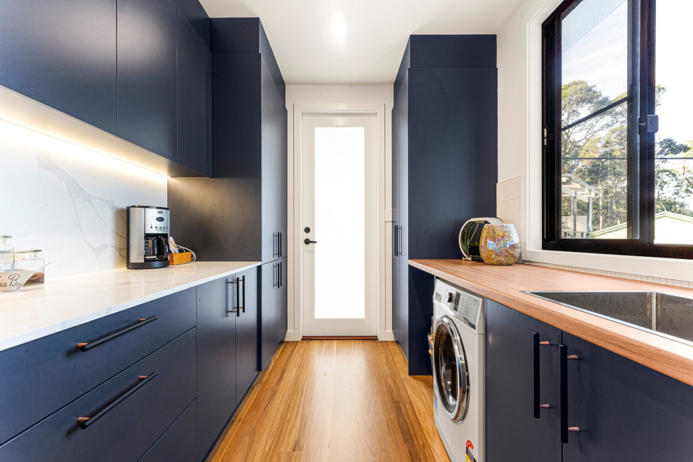 Inspiration for a contemporary galley kitchen pantry in Central Coast with a drop-in sink, flat-panel cabinets, black cabinets, wood benchtops, white splashback, engineered quartz splashback, white appliances, medium hardwood floors, no island, brown floor and brown benchtop.