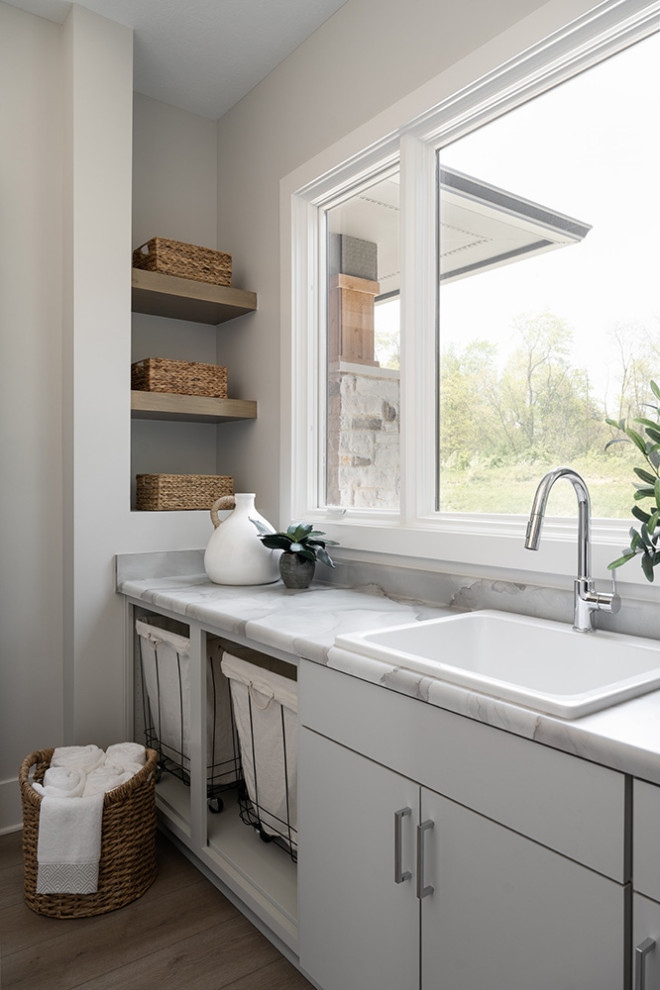 Design ideas for a mid-sized beach style l-shaped dedicated laundry room in Indianapolis with an undermount sink, flat-panel cabinets, beige cabinets, beige walls and medium hardwood floors.