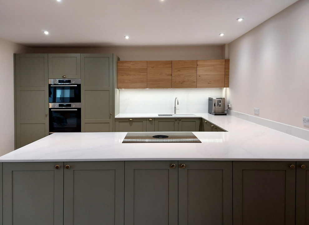 Mid-sized transitional u-shaped open plan kitchen in Other with a double-bowl sink, shaker cabinets, green cabinets, quartzite benchtops, white splashback, engineered quartz splashback, stainless steel appliances, plywood floors, a peninsula, beige floor and white benchtop.