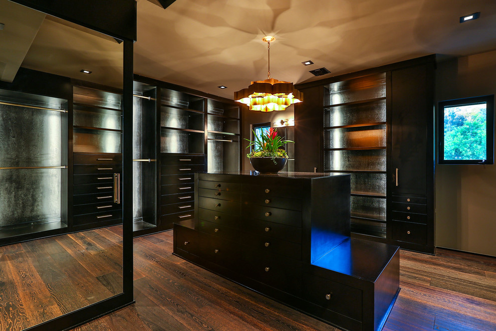 This is an example of a contemporary gender-neutral dressing room in Los Angeles with flat-panel cabinets, dark wood cabinets, dark hardwood floors and brown floor.