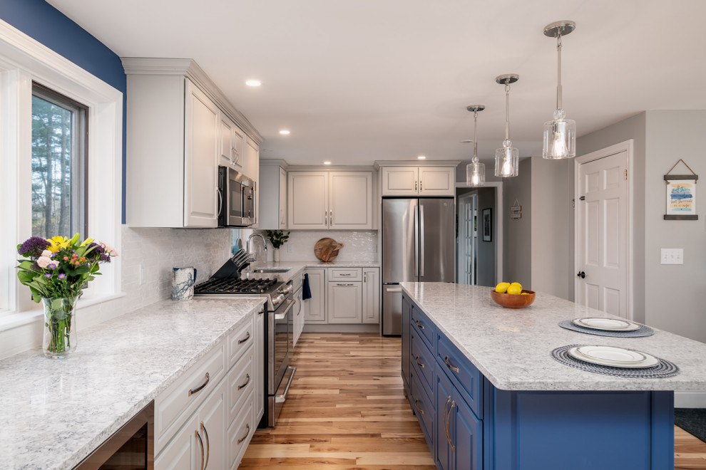 Example of a mid-sized transitional l-shaped light wood floor eat-in kitchen design in Boston with a single-bowl sink, raised-panel cabinets, gray cabinets, quartz countertops, white backsplash, ceramic backsplash, stainless steel appliances, an island and white countertops