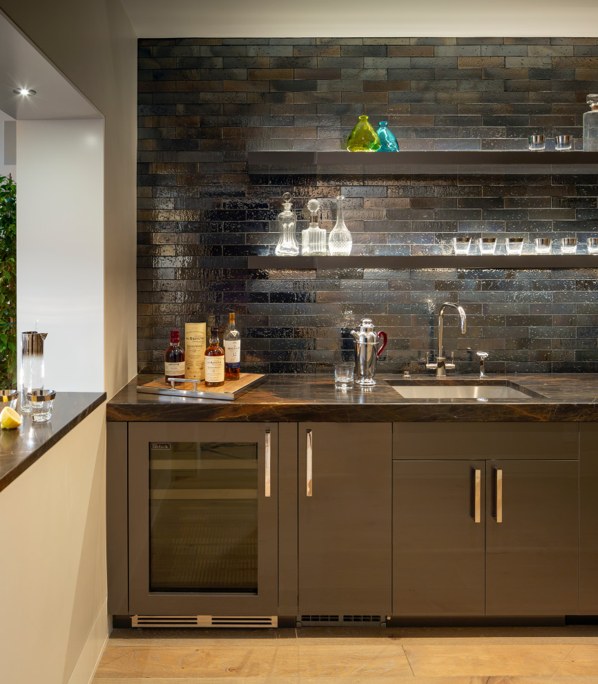 Photo of a large contemporary l-shaped wet bar in San Francisco with an undermount sink, flat-panel cabinets, brown cabinets, marble benchtops, black splashback, ceramic splashback, light hardwood floors, beige floor and brown benchtop.
