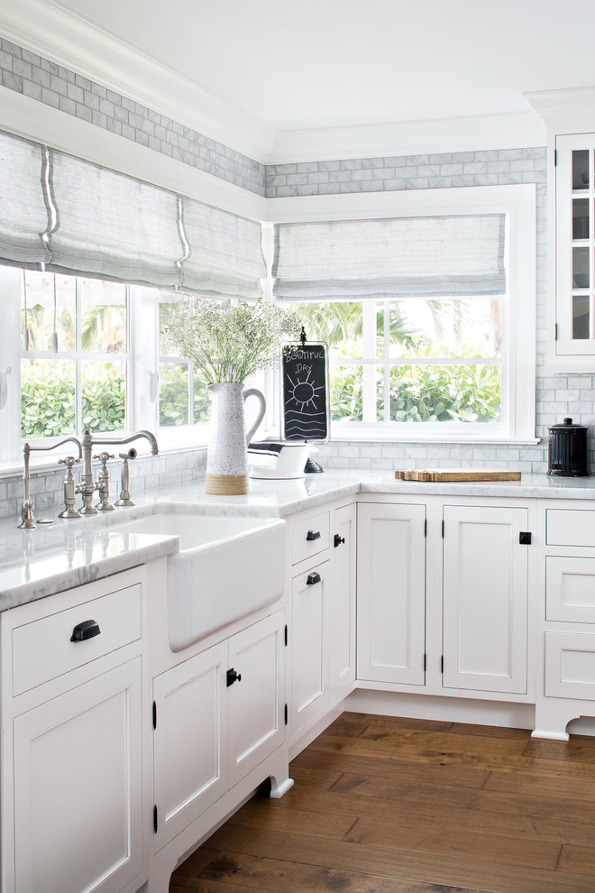 Large beach style l-shaped open plan kitchen in Miami with a farmhouse sink, white cabinets, marble benchtops, grey splashback, marble splashback, panelled appliances, medium hardwood floors, with island, shaker cabinets and brown floor.