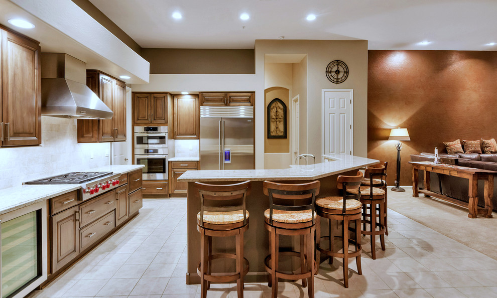 Large transitional l-shaped ceramic tile and white floor open concept kitchen photo in Phoenix with an undermount sink, raised-panel cabinets, medium tone wood cabinets, solid surface countertops, white backsplash, stainless steel appliances and an island