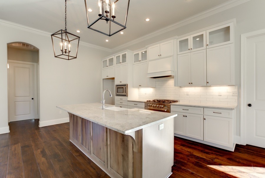 Photo of a mid-sized contemporary galley open plan kitchen in New Orleans with a farmhouse sink, shaker cabinets, white cabinets, granite benchtops, white splashback, subway tile splashback, medium hardwood floors and with island.