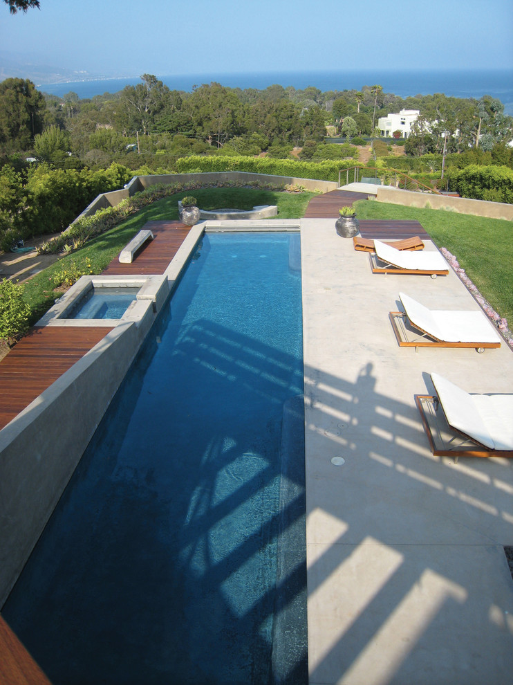 This is an example of a mid-sized modern backyard rectangular lap pool in Los Angeles with a water feature and concrete slab.