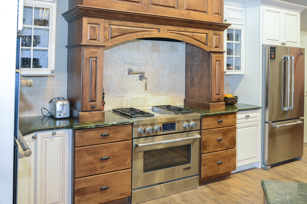 Inspiration for a mid-sized rustic l-shaped light wood floor eat-in kitchen remodel with an undermount sink, raised-panel cabinets, brown cabinets, granite countertops, green backsplash, porcelain backsplash, stainless steel appliances and an island