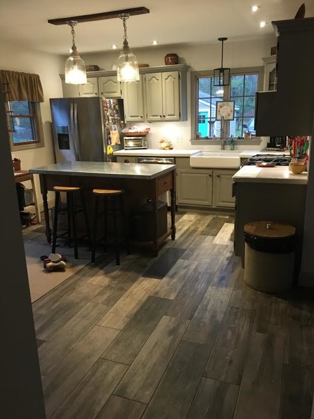 This is an example of a mid-sized country l-shaped eat-in kitchen in New York with a farmhouse sink, raised-panel cabinets, grey cabinets, solid surface benchtops, stainless steel appliances, dark hardwood floors, with island and brown floor.