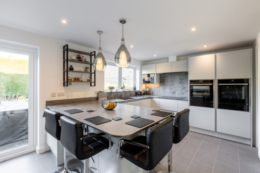 Design ideas for a medium sized contemporary u-shaped open plan kitchen in Sussex with flat-panel cabinets, grey cabinets, quartz worktops, grey splashback, engineered quartz splashback, black appliances and grey worktops.