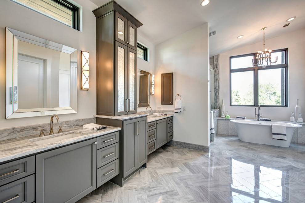 This is an example of an expansive contemporary master bathroom in Austin with an undermount sink, shaker cabinets, grey cabinets, marble benchtops, a freestanding tub, a double shower, a two-piece toilet, gray tile, stone tile, white walls and marble floors.