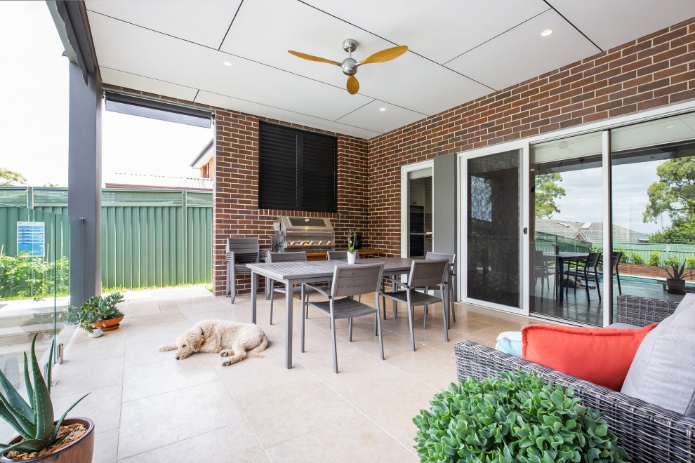 This is an example of a large transitional backyard patio in Sydney with tile and a roof extension.