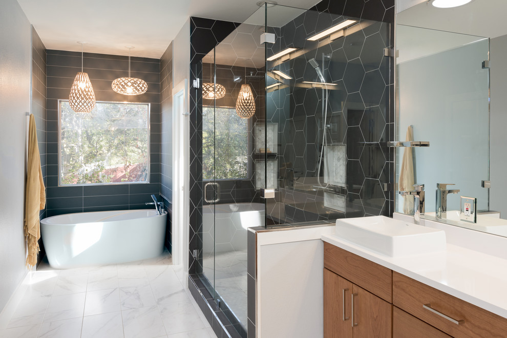 This is an example of a contemporary master bathroom in Austin with flat-panel cabinets, medium wood cabinets, a freestanding tub, a corner shower, black tile, grey walls, marble floors, a vessel sink and a hinged shower door.