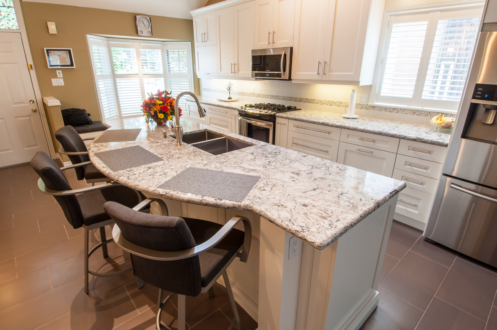 Example of a mid-sized transitional galley ceramic tile eat-in kitchen design in Toronto with a double-bowl sink, shaker cabinets, white cabinets, granite countertops, beige backsplash, stone tile backsplash, stainless steel appliances and an island