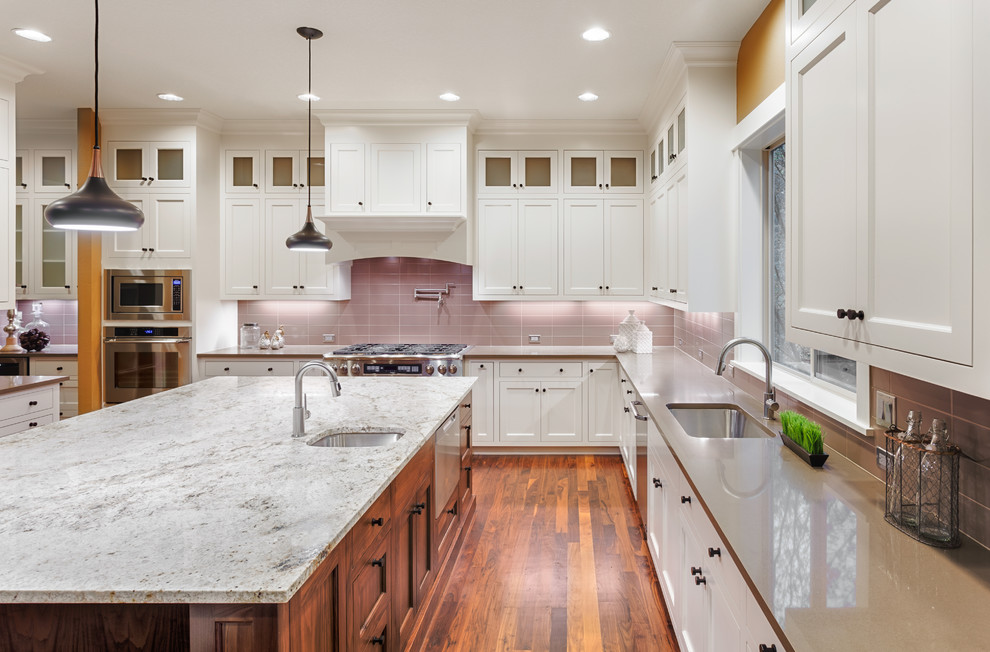 This is an example of a large transitional u-shaped kitchen in San Francisco with an undermount sink, shaker cabinets, white cabinets, quartz benchtops, pink splashback, glass tile splashback, stainless steel appliances, bamboo floors, with island, brown floor and grey benchtop.