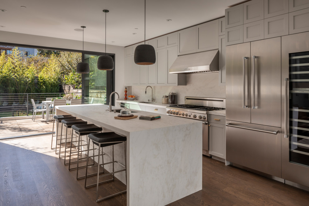 Design ideas for a large transitional galley open plan kitchen in San Francisco with an undermount sink, shaker cabinets, grey cabinets, marble benchtops, white splashback, marble splashback, stainless steel appliances, with island, white benchtop, dark hardwood floors and brown floor.