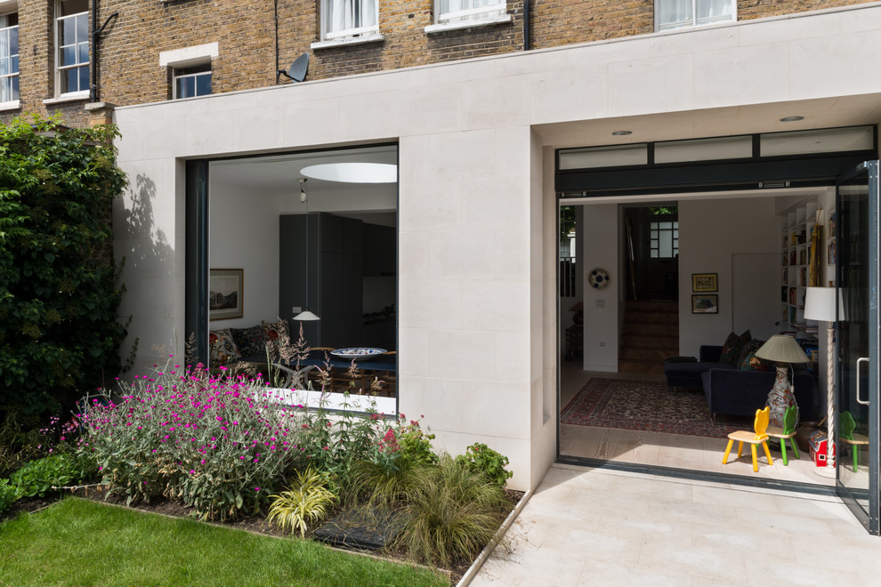 This is an example of a medium sized and beige contemporary house exterior in London with stone cladding and a flat roof.