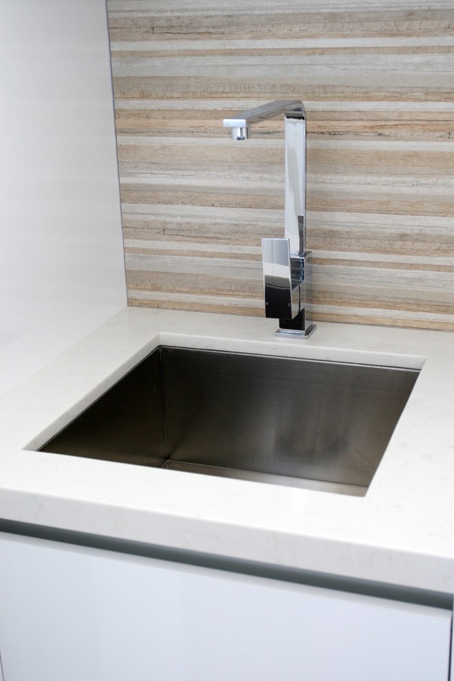 Mid-sized contemporary single-wall utility room in Sydney with an undermount sink, flat-panel cabinets, quartz benchtops, white splashback, glass sheet splashback, dark hardwood floors, white cabinets, brown floor, white benchtop, a concealed washer and dryer and white walls.