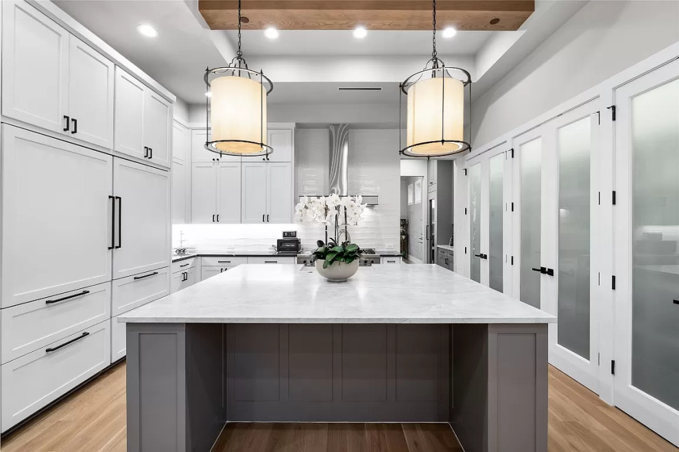 Large transitional u-shaped open plan kitchen in Houston with a farmhouse sink, shaker cabinets, grey cabinets, marble benchtops, grey splashback, porcelain splashback, panelled appliances, light hardwood floors, with island, brown floor and multi-coloured benchtop.