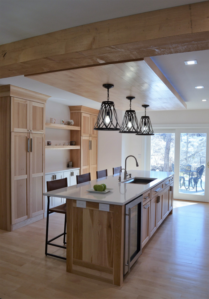 This is an example of a mid-sized country single-wall open plan kitchen in New York with a single-bowl sink, shaker cabinets, light wood cabinets, quartzite benchtops, black splashback, ceramic splashback, stainless steel appliances, light hardwood floors, with island, beige floor, white benchtop and wood.