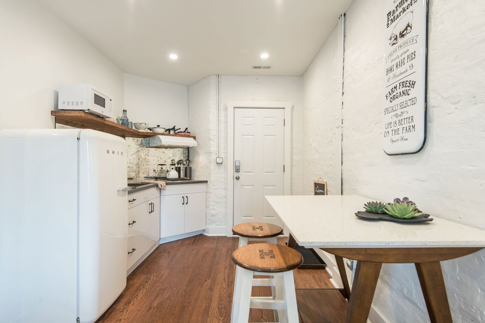 This is an example of a mid-sized contemporary galley eat-in kitchen in Chicago with an undermount sink, flat-panel cabinets, white cabinets, granite benchtops, white splashback, stainless steel appliances, medium hardwood floors, no island and black benchtop.